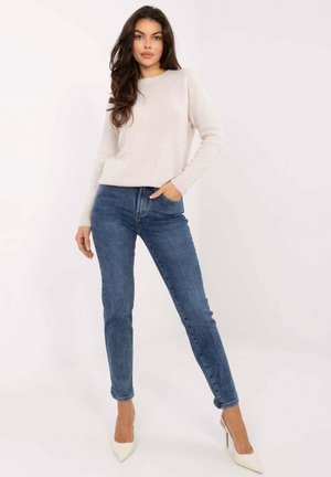Hellbeiger, flauschiger Pullover mit langen Ärmeln, kombiniert mit dunkelblauen Skinny Jeans. Model trägt beigefarbene spitze Pumps; legere Haltung.