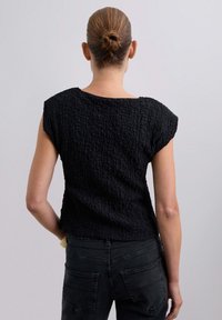 Top nero con texture, caratterizzato da maniche corte e una vestibilità ampia. Il tessuto presenta un design arricciato, abbinato a jeans scuri.