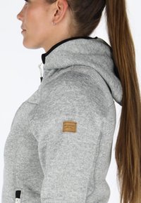 Gray zip-up hoodie with a textured fabric, featuring a hood, contrasting black trim, and a brown leather brand patch on the left shoulder.