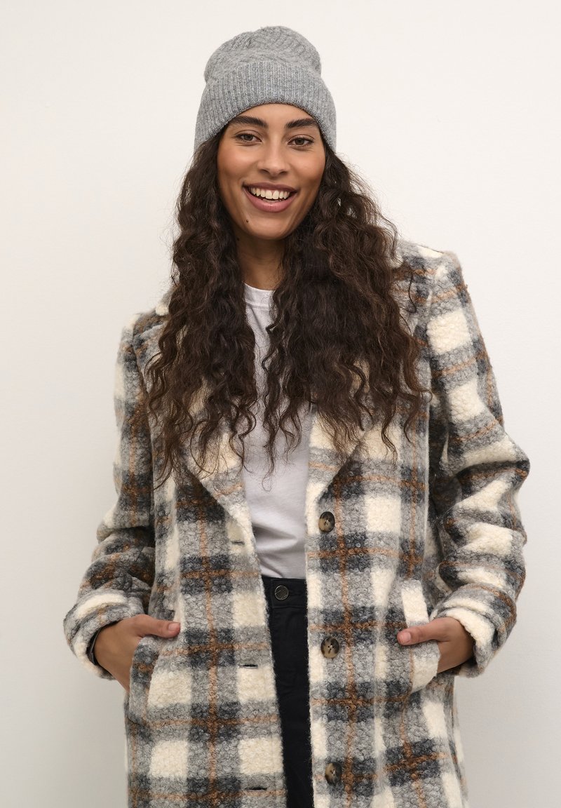 Plaid coat in cream, gray, and brown, made of textured fabric; features large buttons and side pockets. Paired with a gray knitted beanie.