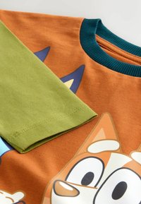 Pomarańczowy bawełniany t-shirt z zielonym rękawem, zdobiony grafiką postaci z kreskówki i turkusowym ściągaczem przy kołnierzyku. Gładka faktura, casualowy design.