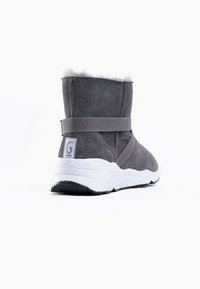 Botines de ante gris con suelas de goma blancas, collar acolchado y detalle de correa horizontal. Textura suave con un forro blando.