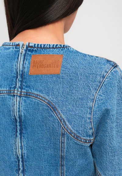 Džínová bunda svetlo modrej farby, s kontrastným oranžovým prešívaním a hnedou koženou značkou na krku.