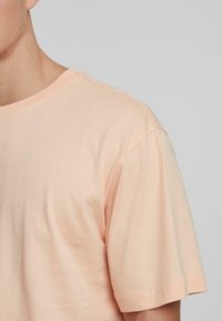 Hellblau pfirsichfarbendes T-Shirt mit rundem Halsausschnitt, kurzen Ärmeln und einer glatten, weichen Textur. Verfügt über doppelt genähte Nähte.