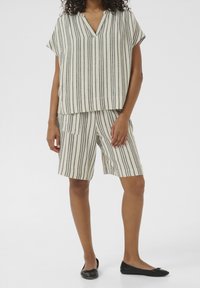 Lichtgewicht gestreept tweedelig outfit bestaande uit een losse, kortmouwen top en bijpassende shorts in neutrale kleuren met verticale zwarte strepen.