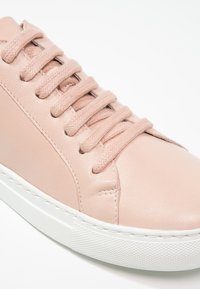Baskets en cuir rose clair avec lacets assortis et semelle épaisse en caoutchouc blanc, vues en gros plan de côté et de face.
