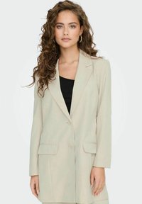 Ljusbeige blazer med skräddarsydd passform, enkel knappstängning, två framfickor, notchlapel och slät tygtextur.
