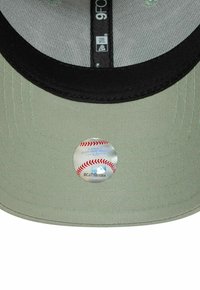 Gorra de béisbol color caqui con visera negra, que presenta una pegatina reflectante con un diseño de béisbol en la parte inferior de la visera.
