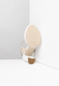 Zapato de tacón alto beige de punta abierta con un tacón bloque blanco, que presenta una suela texturizada y tiras finas alrededor del tobillo. El tacón tiene una punta redondeada y goma.