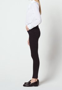 Vaqueros skinny negros combinados con una camisa blanca de manga larga con collar de pajarita. Los zapatos son unos mocasines negros brillantes.