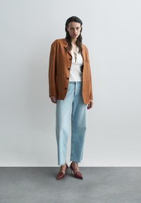 Brun semsket blazer med store knapper, hvit snøring strikket topp, lys blå høyt liv jeans og dyp rød spiss hæler.