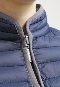 Giacca a vento con esterno blu navy, colletto grigio, texture trapuntata e zip argentata con il nome del marchio "Frieda & Freddies."