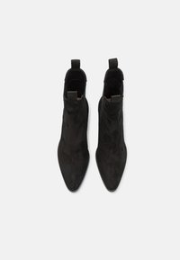 Botines negros de ante con diseño de punta afilada, que presentan lengüetas de tirón y una textura suave. Sin herrajes ni patrones visibles.