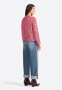 Rosa und mehrfarbiger gestrickter Pullover mit Rundhalsausschnitt, kombiniert mit hochgeschnittenen blauen Jeans, aufgerollten Säumen und braunen Stiefeletten mit Absatz.