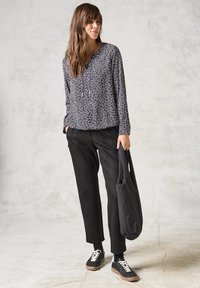 Blusa nera a maniche lunghe con motivo di foglie bianche, abbinata a pantaloni neri a vita alta e sneakers nere con suola bianca. Borsa a spalla nera.
