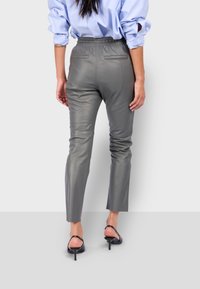 Upnuté šedé kožené kalhoty s elastickým pasem, zúženými nohavicemi, dvěma zadními kapsami a hladkým povrchem. Nosit s černými sandály na podpatku.