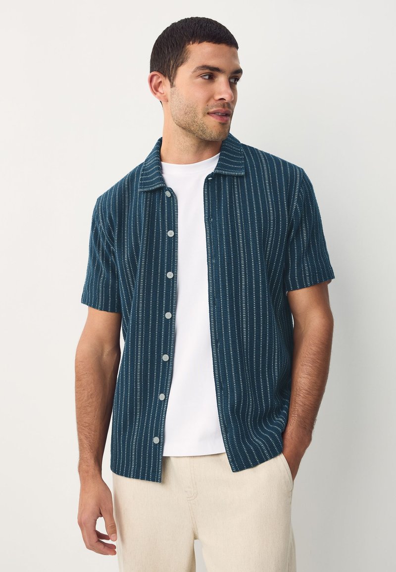 Short-sleeve, collared shirt in dark teal with vertical white stripes. Made from a textured fabric, featuring a button closure and a relaxed fit.