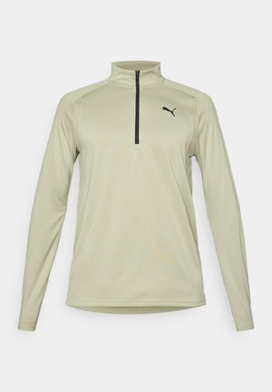Kreemikas pikkade varrukatega spordipluus, millel on must poolik tõmblukk ja väike must Puma logo vasakul rinnal.