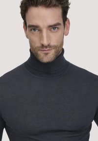 Marineblauwe coltrui gemaakt van zachte stof met een getailleerd ontwerp. Heeft een geribbelde kraag en manchetten, met een gladde textuur zonder zichtbare patronen.