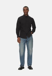 Maglietta nera a maniche lunghe con bottoni frontali, abbinata a jeans dritti blu chiaro e scarpe nere lucide. Design semplice, senza motivi visibili.