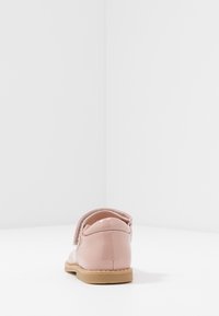 Zapato de charol rosa con puntera redondeada, tira de velcro y suela de goma color beige; textura suave con un acabado brillante.