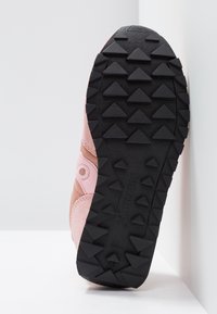 Chaussure de sport avec une tige en suède rose et beige, dotée d'une semelle en caoutchouc avec des crampons triangulaires proéminents pour l'adhérence.