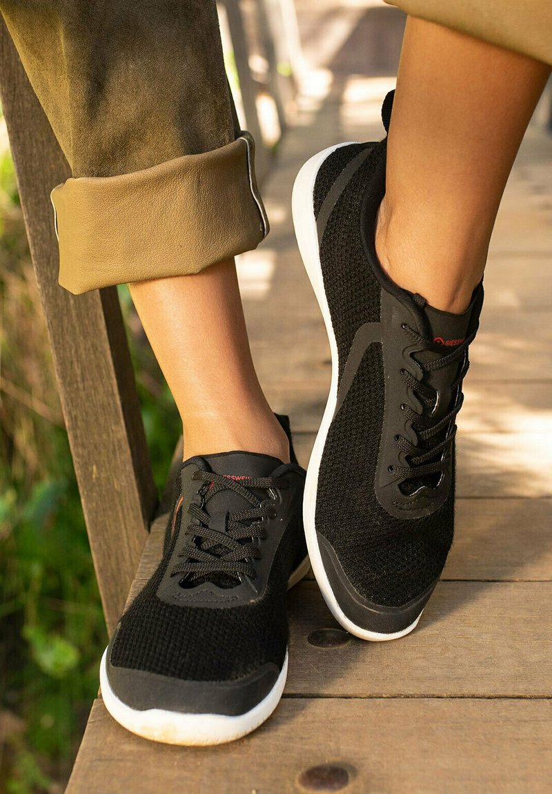Black athletic shoes feature a breathable mesh upper and rubber soles, with black laces and a white midsole, resting on a wooden surface.