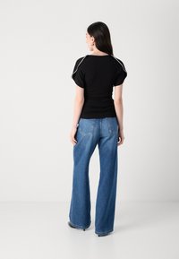 Black short-sleeve top with white piping, paired with high-waisted blue wide-leg jeans, featuring back pockets and a relaxed fit.