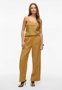 Top sin mangas de color mostaza con escote en V, combinado con pantalones de pierna ancha. Textura suave, diseño minimalista y un ajuste relajado. Tacones negros.