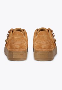 Jasnobrązowe zamszowe sneakersy z masywną gumową podeszwą. Posiadają dekoracyjne sznurowanie i wytłoczone logo z tyłu. Gładka tekstura z minimalnymi akcentami.