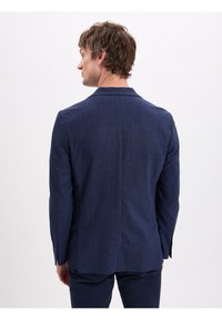 Navyblauwe blazer van een gestructureerde stof, met een notch lapel, enkele split en twee achterzakken. Tailored fit met lange mouwen.