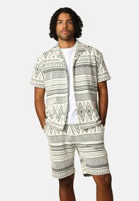 Korte mouwen met een patroon en bijpassende shorts in beige met zwarte geometrische ontwerpen. Lichtgewicht stof met een ontspannen pasvorm.