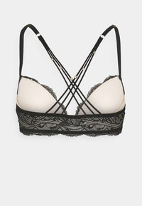 Reggiseno in pizzo nero con spalline regolabili e design incrociato. Coppe morbide imbottite e ornamenti in pizzo intricati lungo i bordi.