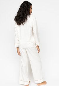 Weißes Baumwoll-Pyjama-Set mit langärmeligem Oberteil mit Rundhalsausschnitt und passenden weit geschnittenen Hosen mit kontrastierendem Saum an den Bündchen.