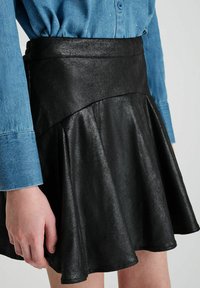Zwarte neplederen skaterrok met een aansluitende taille en een uitlopende zoom. De textuur lijkt glad met een lichte glans.