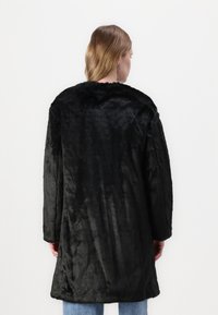 Črna plašč iz umetnega krzna z mehko teksturo, dolgimi rokavi in sproščenim krojem, z okroglo izrezom in srednje dolgim dizajnom.