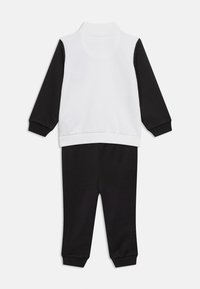 Παιδική φόρμα με μακριά μανίκια, λευκό μπλουζάκι και μαύρα μανίκια, συνδυασμένη με μαύρο παντελόνι, σε λευκό φόντο.