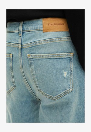 Lichtblauwe denim jeans met een strak ontwerp, voorzien van een leren label met de tekst "The Kooples" en subtiele distressed details aan de achterkant.