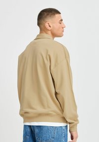 Beige oversized sweatshirt met een ronde hals, geribbelde manchetten en zoom, gecombineerd met lichtblauwe denim jeans. Zachte stof en ontspannen pasvorm.