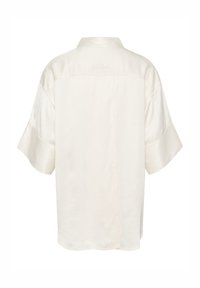Camicia a maniche corte color crema, caratterizzata da una texture morbida, un colletto classico e un dettaglio con cucitura curva sul retro.