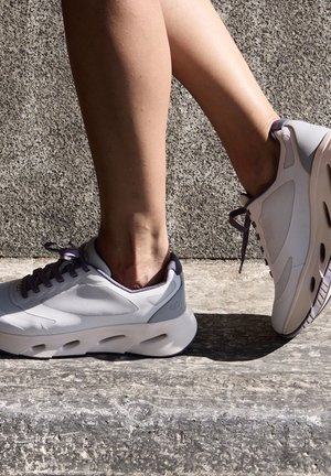 Baskets de sport gris clair avec une tige en mesh lisse, des lacets sombres et une semelle rembourrée dotée d'ouvertures pour la respirabilité.