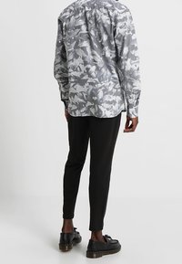 Chemise à manches longues grise avec un motif abstrait blanc, associée à un pantalon noir slim et des chaussures noires à lacets. Tissu lisse, coupe ajustée.