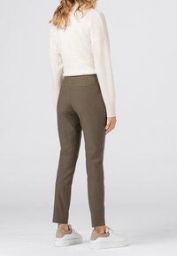 Pantalon olive ajusté avec une texture lisse, poches arrière et longueur cheville, associé à un pull crème clair et des baskets blanches.