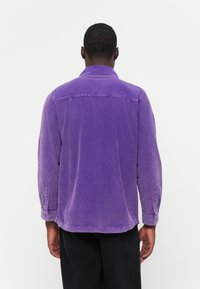 Purple corduroy shirt with long sleeves, a pointed collar, and buttoned cuffs. Back view shows yoke stitching and a slightly faded texture.