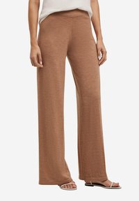 Bruine wijde broek van zacht, textuurstof, met een hoge taille en een ontspannen pasvorm, gecombineerd met minimalistische platte sandalen.
