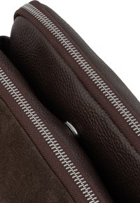 Primo piano di due borse in pelle e camoscio marrone scuro con chiusure lampo in metallo argentato.