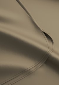 Nahaufnahme von glattem, gefaltetem taupefarbenem Stoff mit sichtbarem Doppelnähte entlang der gewölbten Kante.