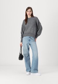 Šedý pletený svetr s převislými rameny, světle modré široké džíny a bílé tenisky. Model také drží malou černou kabelku.