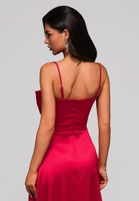 Abito in satin rosso con spalline sottili, corpino aderente e gonna fluente. Presenta una zip sul retro e una texture liscia, che valorizzano il design elegante.