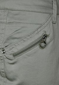 Grå tygbyxor med en liten zip-ficka med en cirkulär metalldragare, kontrasterande sömmar och en mjuk textur.